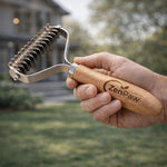 Hand holding a wooden pet grooming tool with 'ZenPaw' branding outdoors.  CoatRake By ZenPaw
